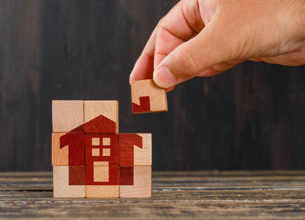 A hand placing a building block for a puzzle of a house
